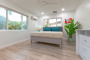 Un dormitorio con cama, una mesita de noche, una planta en maceta, una ventana y un ventilador de techo.