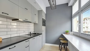 Une cuisine moderne avec des meubles blancs, un plan de travail noir et une fenêtre donnant sur les bâtiments environnants.