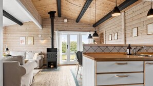 A cozy cabin interior with a wood-burning stove, a dining area, and a kitchen with a sink and cabinets. - Stunning home in Aabenraa (Aabenraa)