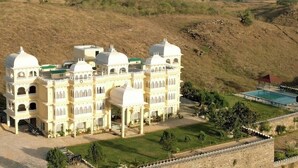 A large, multi-story building with domed roofs and arched windows, surrounded by a well-maintained lawn and a swimming pool.