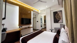 A modern hotel room with a flat-screen TV, a wooden vanity, a bed with a white and brown bedspread, a ceiling fan, and a painting on the wall.