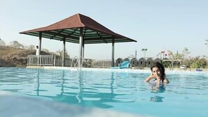A swimming pool with a pavilion, lounge chairs, and a small building in the background.