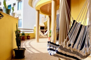 Un hamac suspendu à un balcon, avec des plantes en pot et un escalier en colimaçon en arrière-plan.