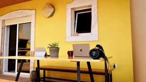 A yellow wall with a window, a door, and a table with a laptop, a plant, and a mug. - Spacious Penthouse w/ Barbecue, wifi, 2 terraces & Views (Praia)