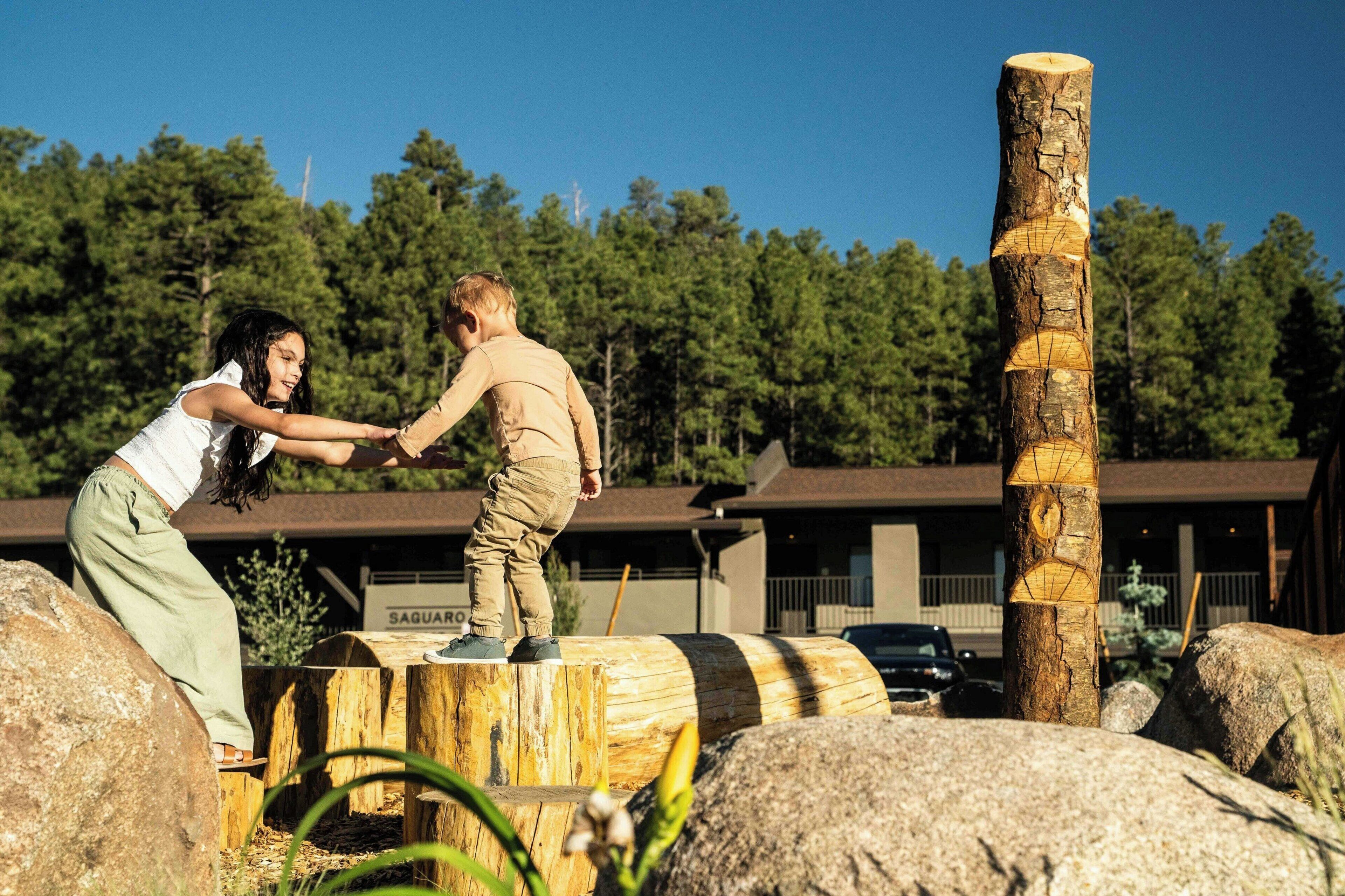 A person standing on a wooden platform with a tree stump, surrounded by rocks and a building in the background.