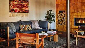 Een gezellige woonkamer met een donkerblauwe bank, een houten salontafel en een open haard.