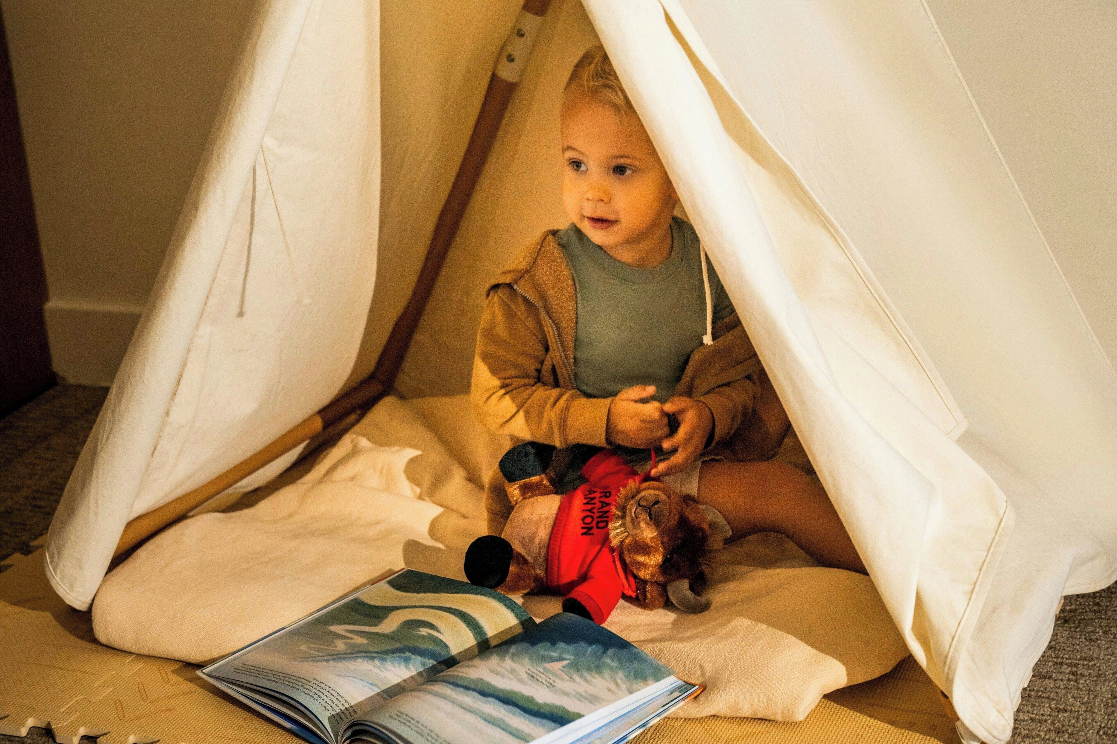 A child in a tent-like structure with a book and a toy on the floor.