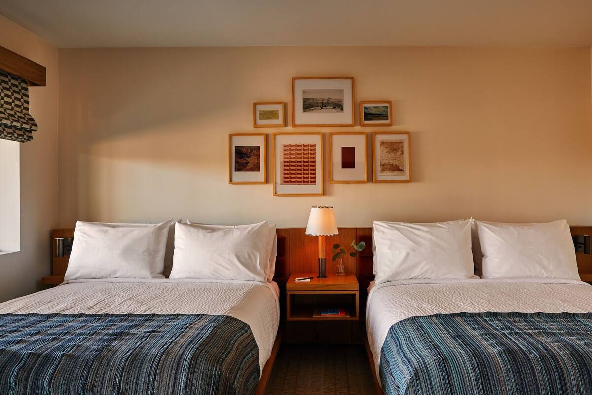 Une chambre d’hôtel avec deux lits, une table de chevet avec une lampe et un mur décoré de tableaux encadrés.