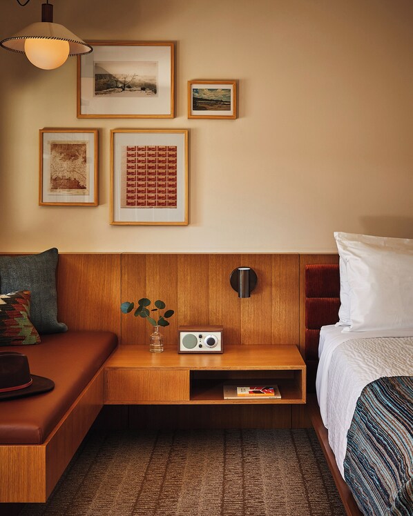 A hotel room with a wooden headboard, a bedside table with a radio, a small plant, and a framed picture collection on the wall. - Trailborn Grand Canyon, Outdoor Collection by Marriott Bonvoy (Williams)