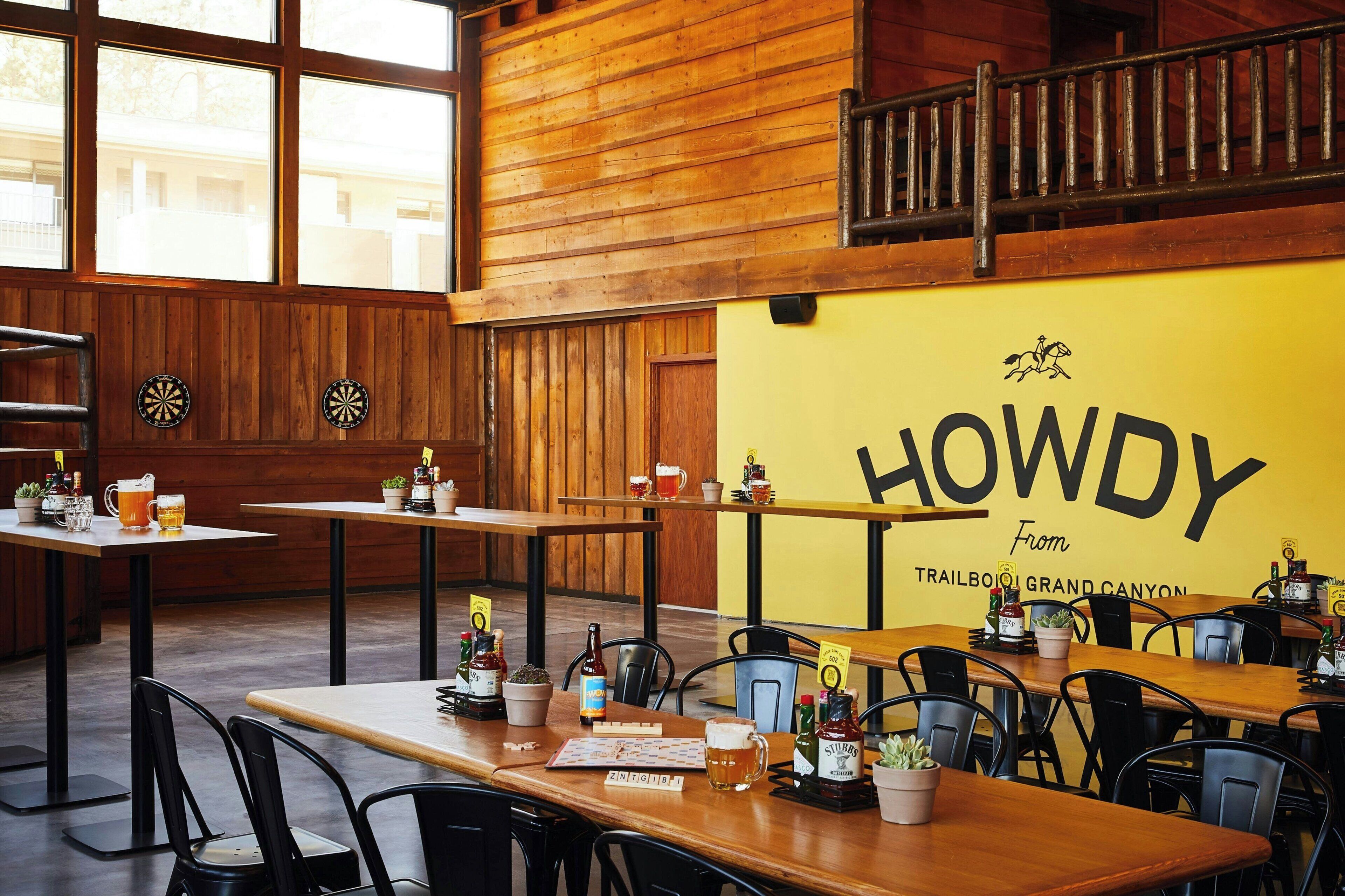 A restaurant interior with wooden walls, tables with chairs, and a large sign reading 'HOWDY From TRAILBOI GRAND CANYON'.