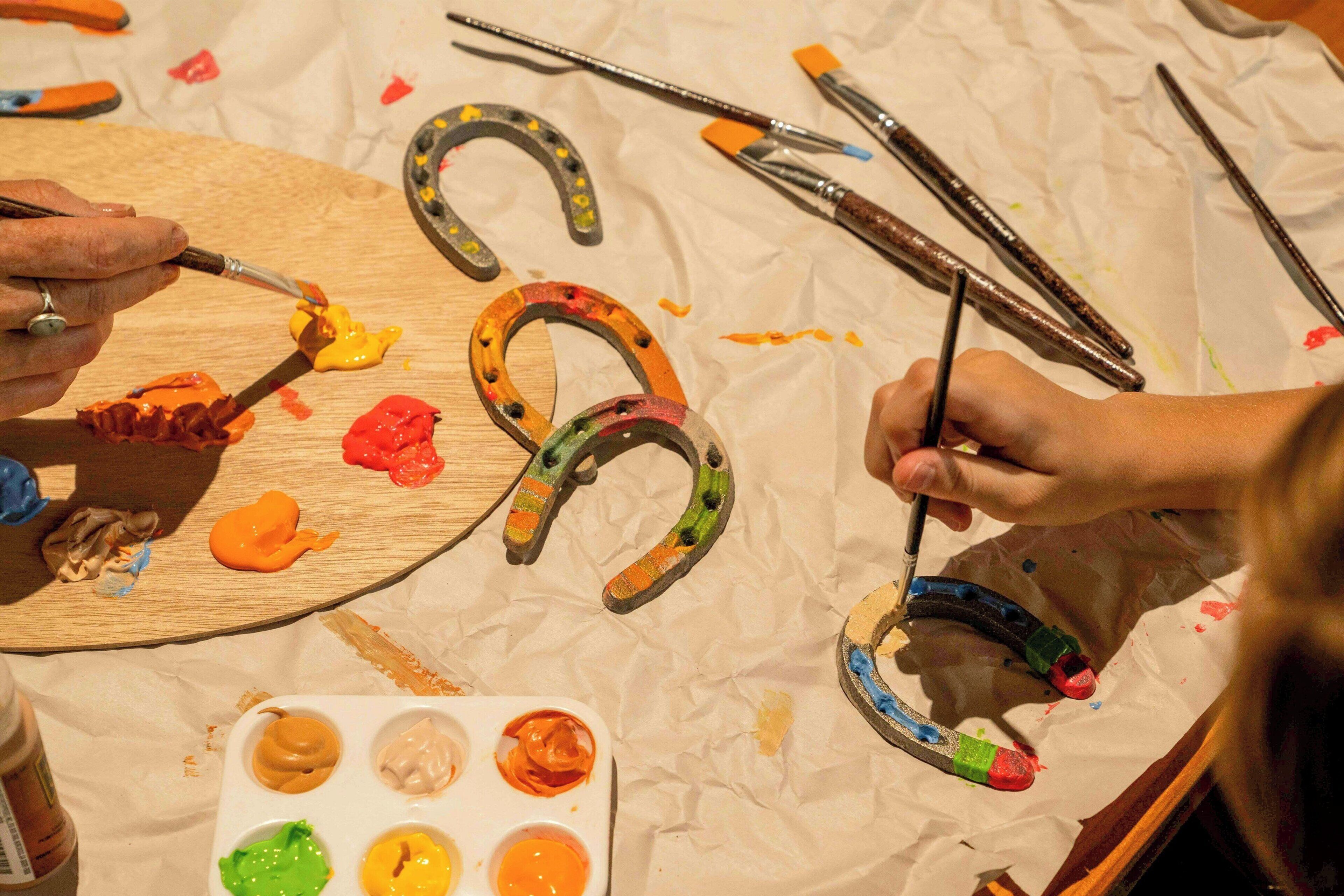 A person painting horseshoes on a wooden surface with various paint colors and brushes.