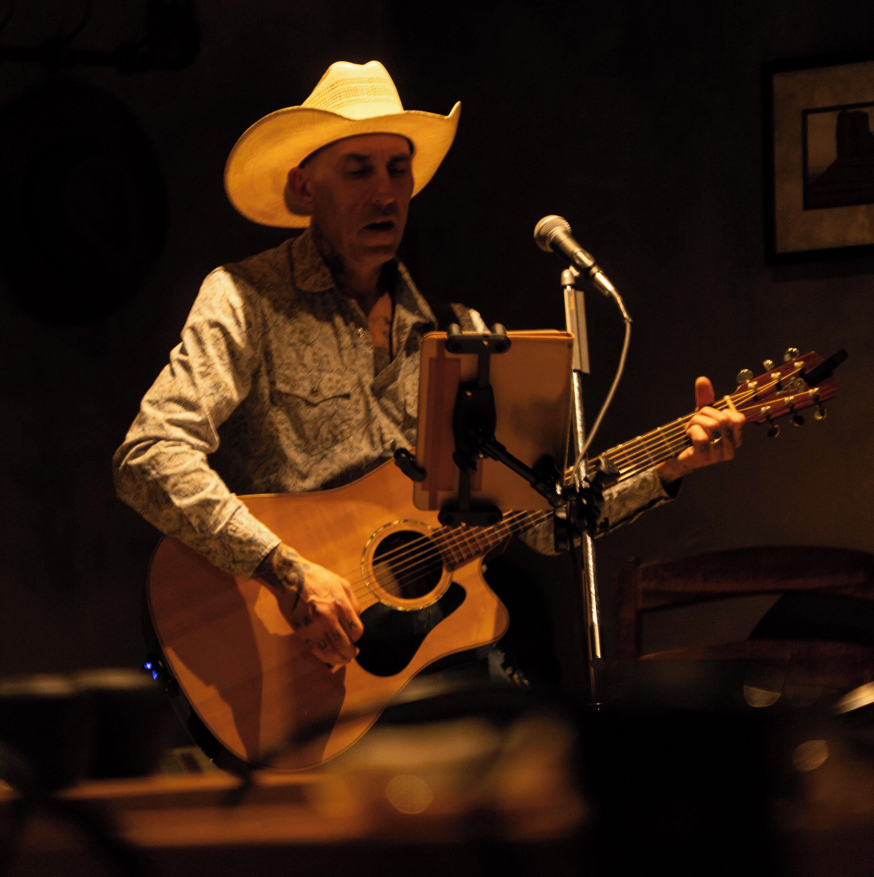A person playing an acoustic guitar on a stage with a microphone stand.