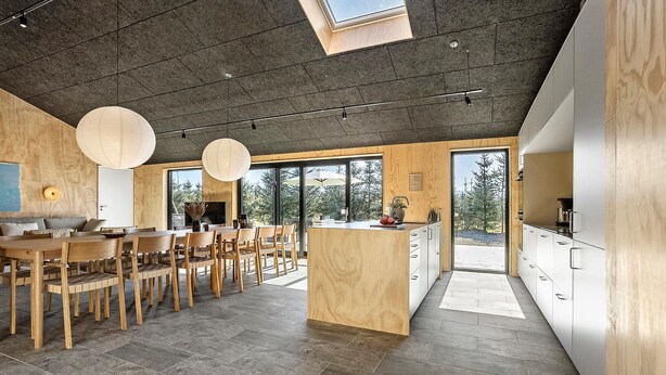 Une cuisine moderne avec des meubles en bois, un îlot central et de grandes fenêtres donnant sur l’extérieur.