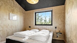 Une chambre à coucher avec un lit, une fenêtre donnant sur des arbres, une table de chevet et un luminaire fixé au mur.