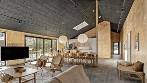 Un vaste espace de vie doté d’un grand téléviseur, de meubles en bois et d’une cuisine située à l’arrière-plan.