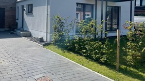 Una casa moderna de dos pisos con techo inclinado, ventanas grandes y un balcón visible.