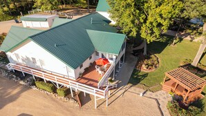 A two-story house with a green roof, a covered porch with outdoor seating, and a fenced yard. - "The Lodge" GREAT FOR GROUPS & Walk-in Norfork River Access in Norfork, AR (Norfork)