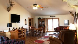 A cozy living room with a ceiling fan, a fireplace, a dining area, and a mounted deer head. - "The Lodge" GREAT FOR GROUPS & Walk-in Norfork River Access in Norfork, AR (Norfork)