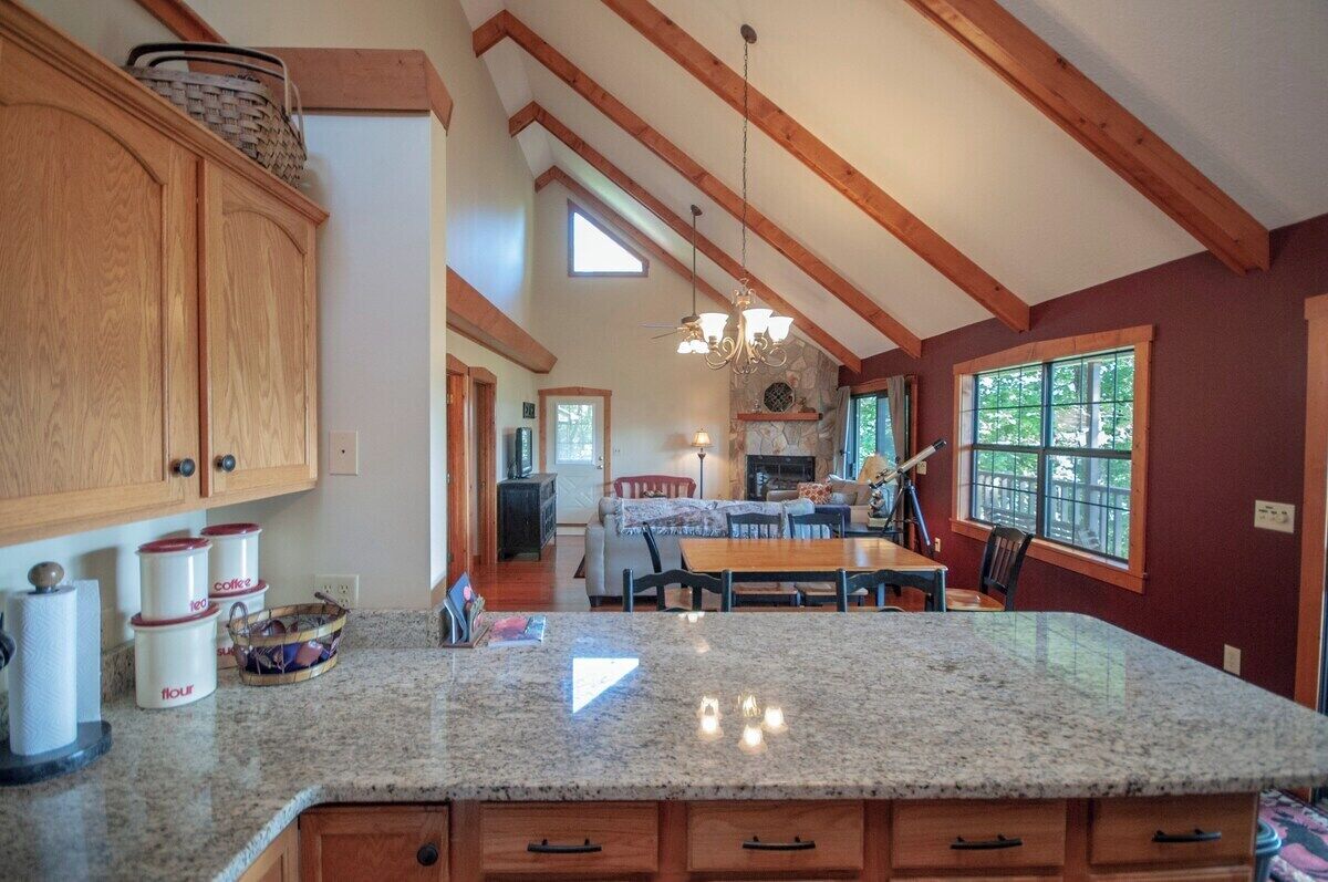 A spacious kitchen with granite countertops, wooden cabinets, and a high ceiling with exposed beams.