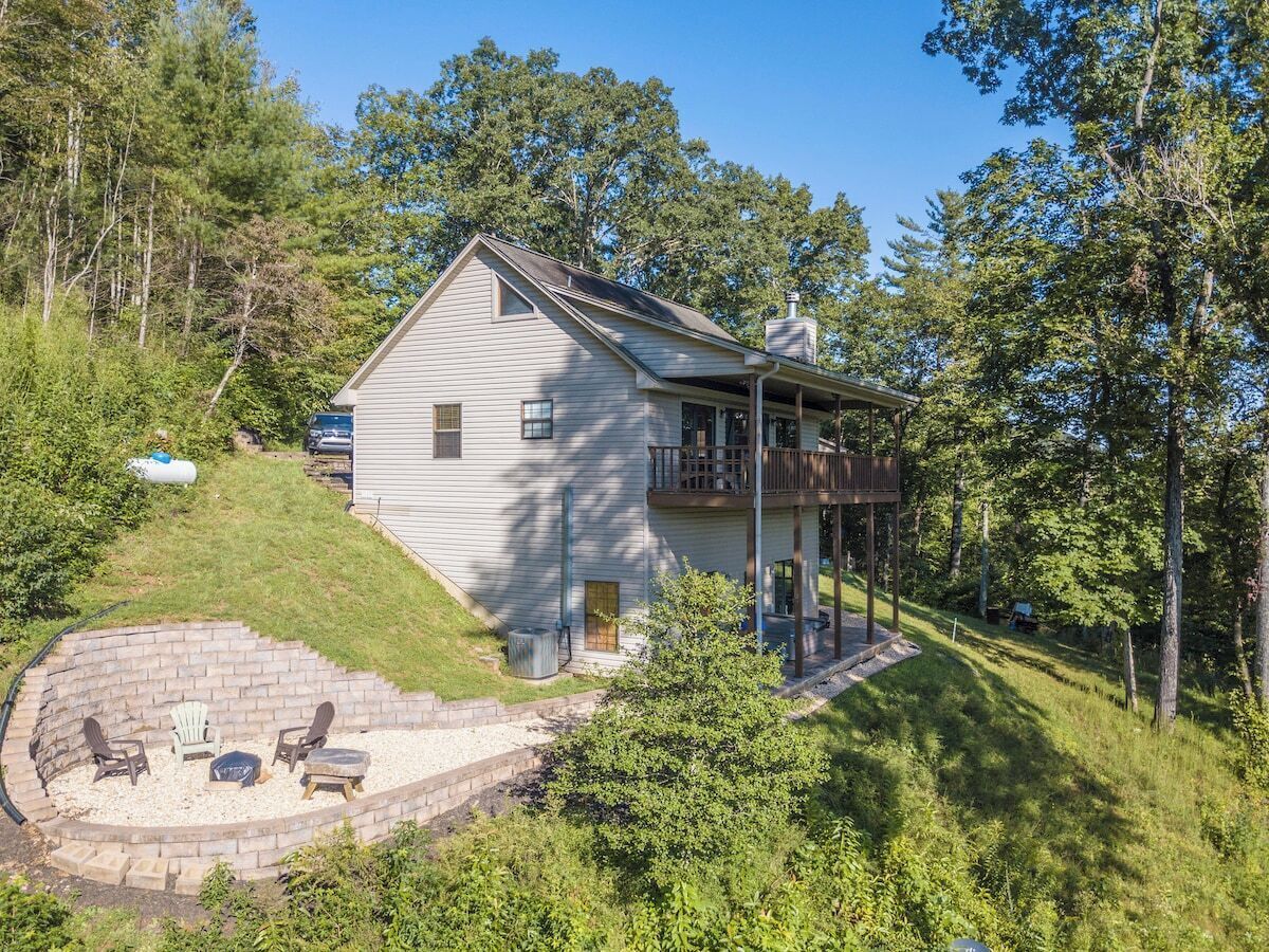 A two-story house with a covered porch and a stone fire pit area.
