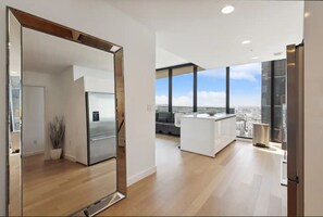 Experience the urban lifestyle in this modern apartment, featuring a spacious kitchen with a stainless steel refrigerator and kitchen island, a large window with city views, and a light-colored floor.