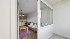 Un espacio habitable compacto con kitchenette, un sofá, una mesita y un tapete morado.