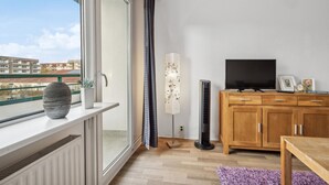 Una sala de estar moderna con un gran ventanal, un televisor de pantalla plana, un mueble de madera y una lámpara de pie.