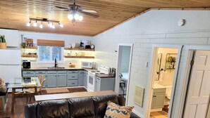 A cozy living room with a leather couch and a dining table, a kitchen with white cabinets and a microwave, and a ceiling fan with lights. - Pinescape: Cabin•WiFi•Wood Fireplace•Pet friendly•Fish•Relaxation (Big River)
