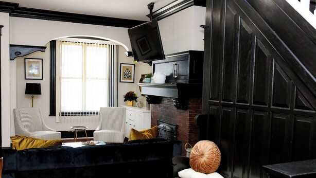 A living room with a black sofa, striped armchairs, a small table, and a fireplace.