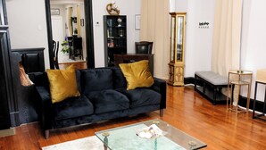 A living room with a black sofa, a glass coffee table, and a wooden floor.