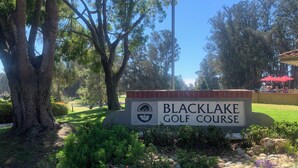 Un panneau indiquant l’emplacement du terrain de golf de Blacklake, entouré d’arbres et bordé d’un jardin bien entretenu.