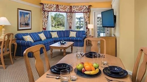 A cozy room with a blue sofa, a dining table set with plates and fruit, and a TV mounted on the wall. - Fantastic condo in Orlando; fully equipped kitchen, washer/dryer, WiFi (Orlando)