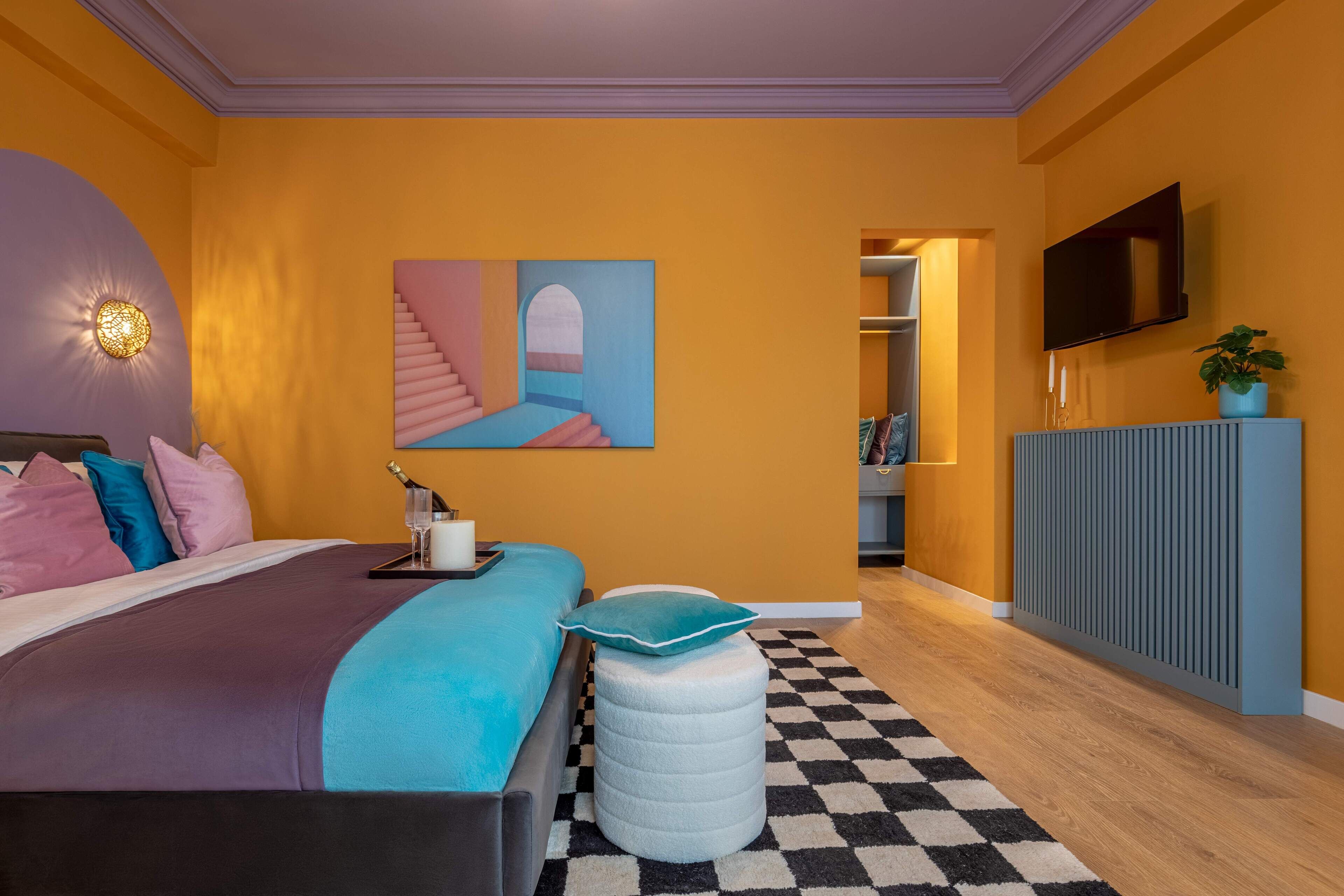 A bedroom with a bed, a painting, a television, and a plant.