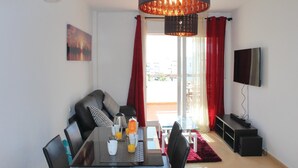 A modern living room with a dining area, a large window with red curtains, a flat-screen TV, and a ceiling light fixture. - Cozy apartment in Torre Pacheco with WiFi (Torre Pacheco)