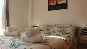 A hotel room with a bed featuring floral bedding, two rolled towels on the bed, a nightstand with a lamp, and a painting of the Eiffel Tower on the wall. - Cozy apartment in Torre Pacheco with WiFi (Torre Pacheco)