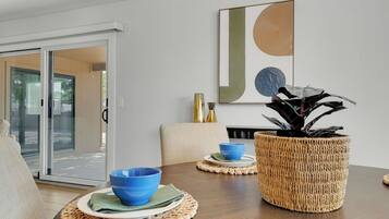 A dining area with a wooden table, blue bowls, a woven basket, and a wall-mounted abstract painting.