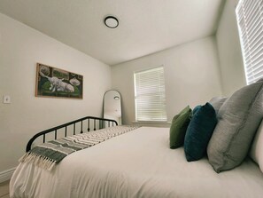 A bedroom with a bed, a painting, a window with blinds, and a ceiling light.
