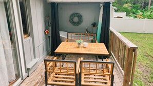 Una terraza de madera con una mesa y sillas, un espacio de patio cubierto y vistas al jardín trasero.