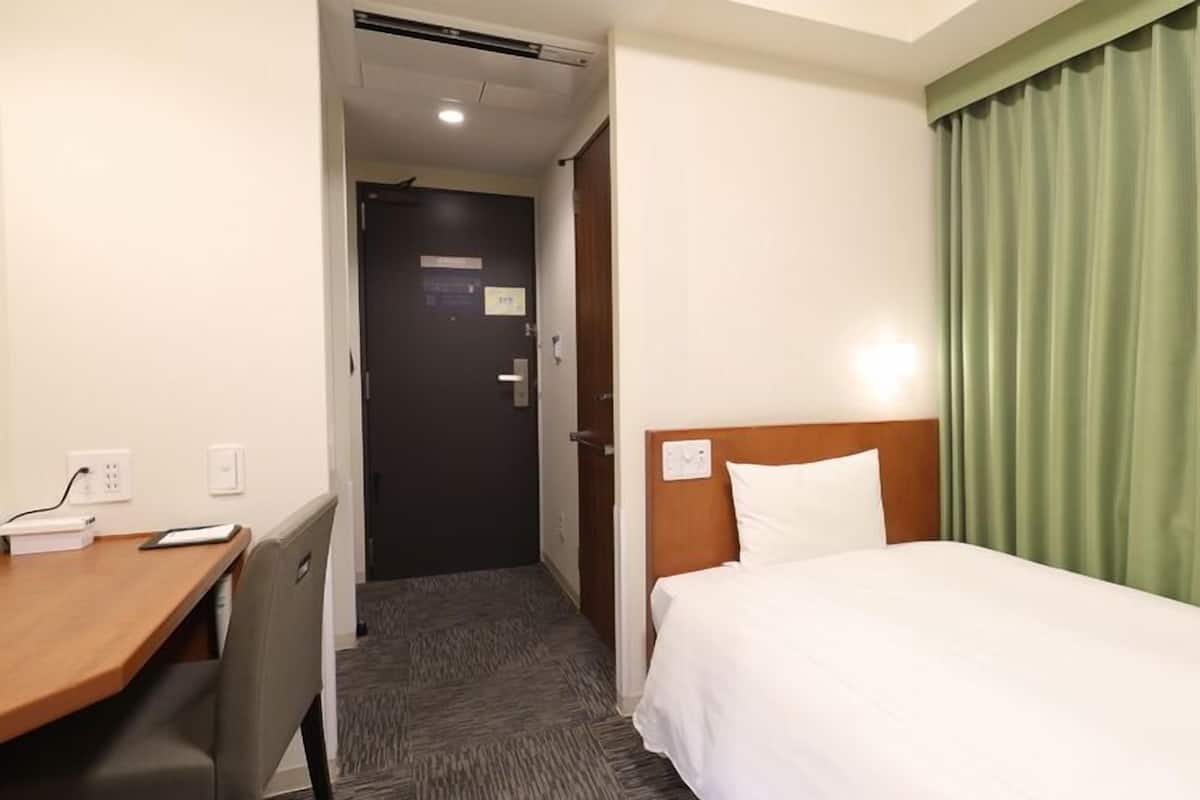 A hotel room with a bed, a desk, and a door.