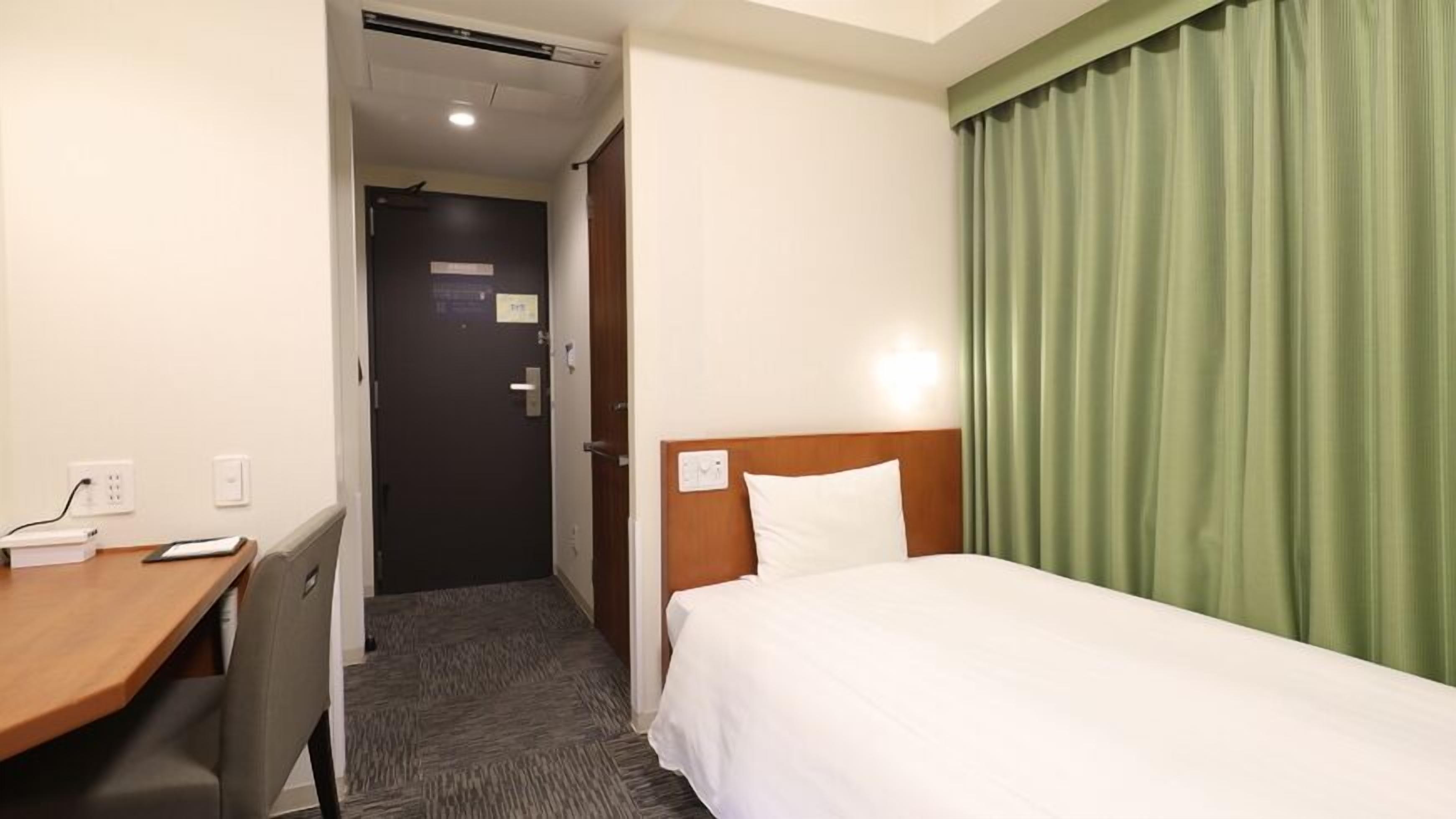 A hotel room with a bed, a desk, and a door.