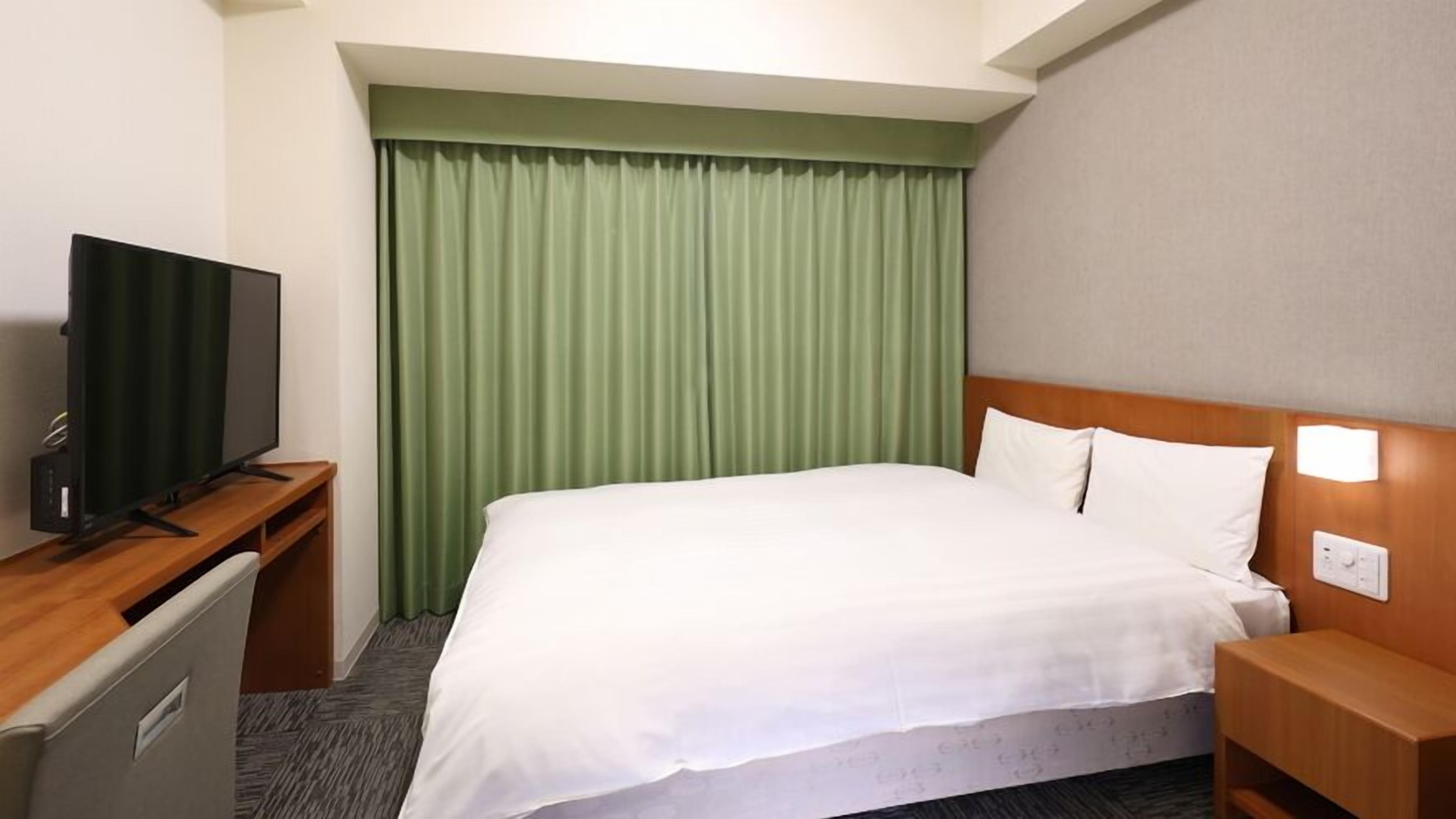 A hotel room with a bed, a television on a desk, and a green curtain.