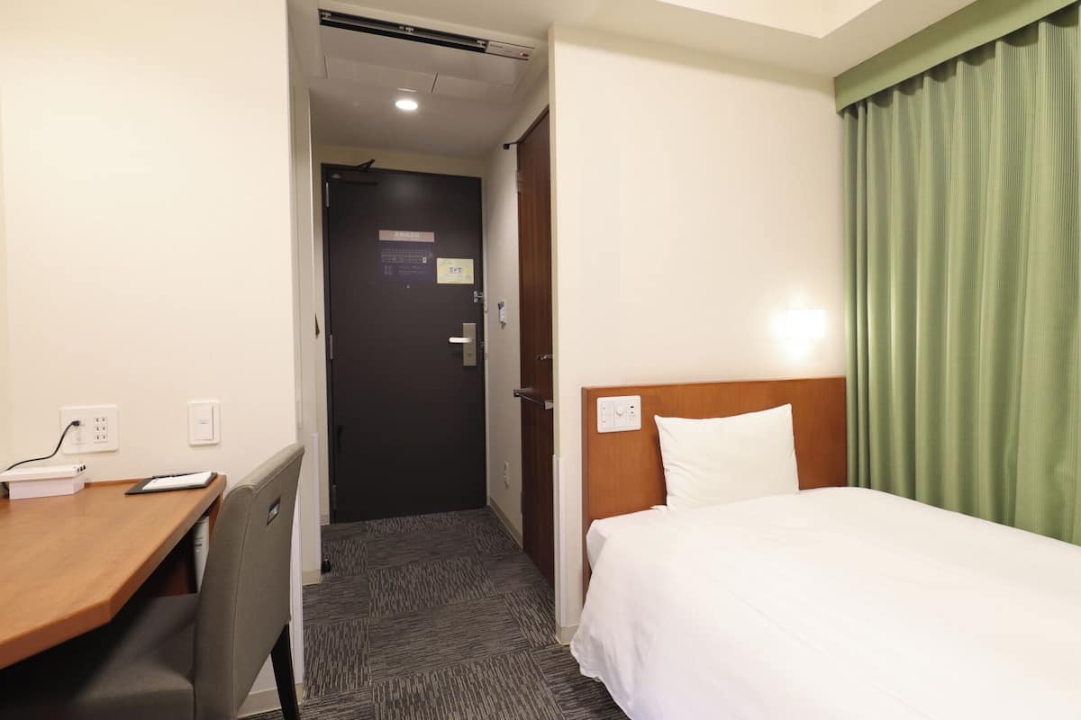 A hotel room with a bed, a desk, and a door leading to a hallway.