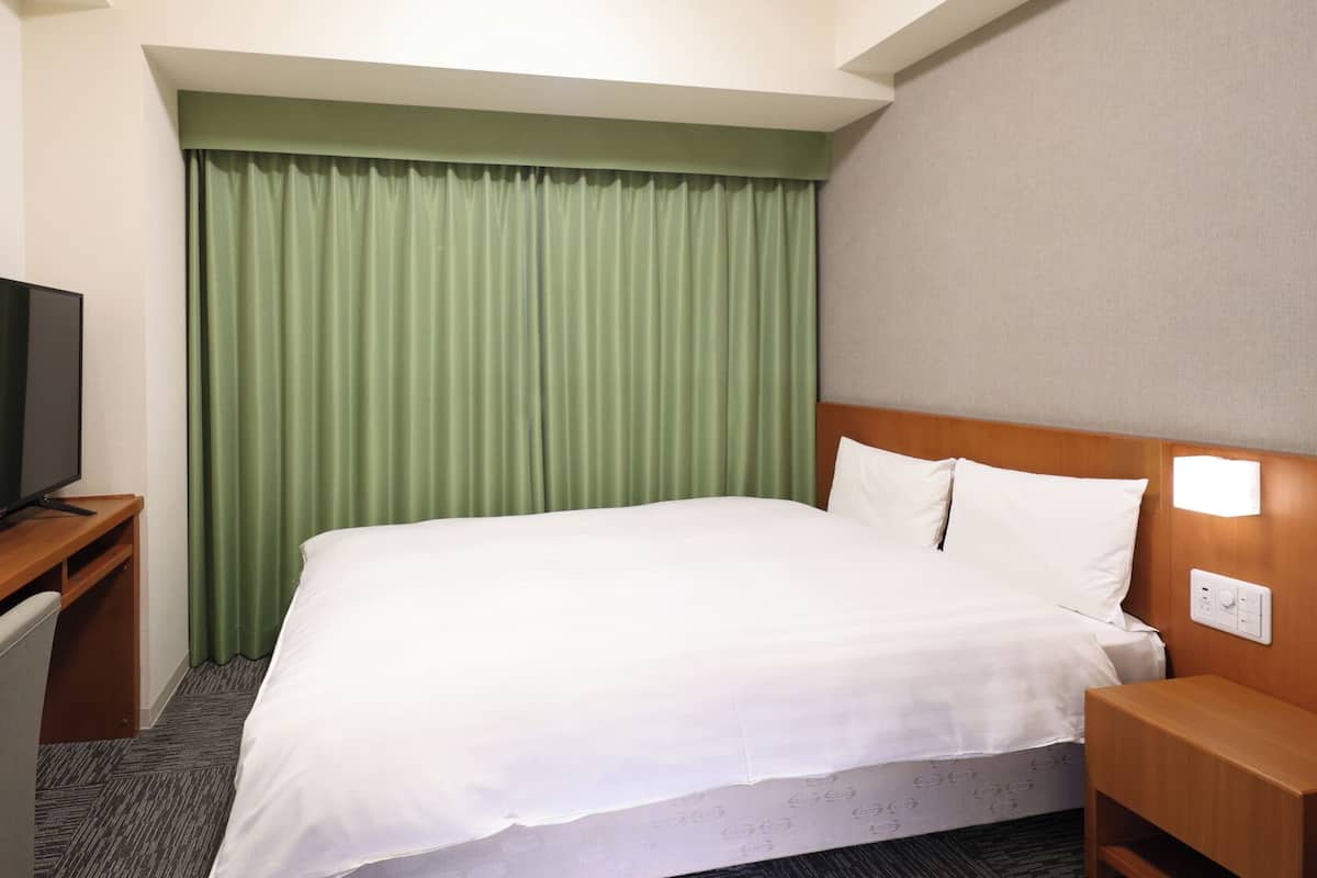 A hotel room with a bed, a TV on a desk, and a green curtain.