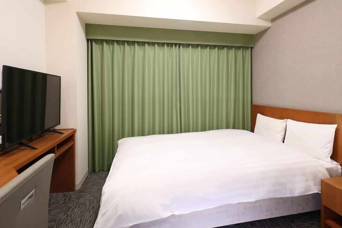 A hotel room with a bed, a television on a desk, and a green curtain.