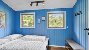 Un dormitorio con dos camas, dos ventanas, un banco y una lámpara en el techo.