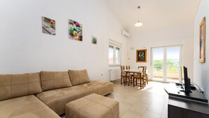 A living room with a beige sofa, a dining table with chairs, and a balcony with a view. - 1 bedroom beautiful apartment in Krusevo (Krusevo)