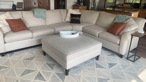 Ein modernes Wohnzimmer mit einem beigefarbenen Ecksofa, einem weißen Couchtisch und einem Teppich mit geometrischem Muster.