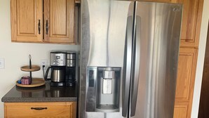 Ein Kühlschrank aus Edelstahl mit Wasserspender, eine Kaffeemaschine und Holzschränke in einer Küche.