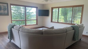 Ein Wohnzimmer mit einer gebogenen Eckcouch, großen Fenstern, einem Deckenventilator und einem flachbildschirmfernseher an der Wand.
