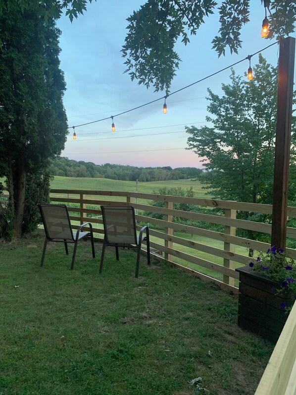 Eine Holzterrasse mit zwei Stühlen, einer Lichterkette und Blick auf ein grünes Feld.